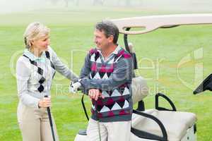 Happy golfing couple with golf buggy behind