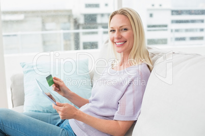 Happy woman with digital tablet and credit card on sofa