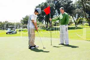 Golfer holding hole flag for friend putting ball