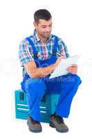 Handyman writing on clipboard while sitting on toolbox