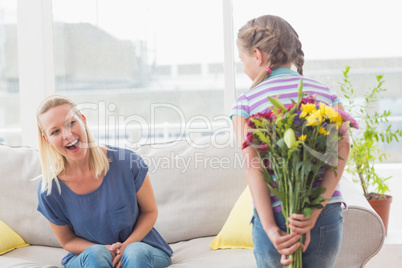 Surprise mother looking at girl hiding bouquet