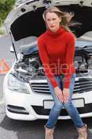 Annoyed young woman beside her broken down car