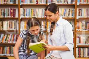 Teacher and girl reading book in library