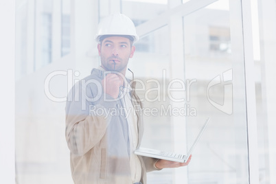 Architect holding laptop while looking away in office