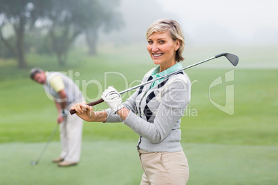 Lady golfer smiling at camera with partner behind