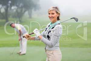 Lady golfer smiling at camera with partner behind