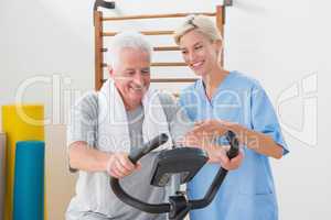 Senior man doing exercise bike with therapist