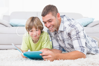 Father and son reading book while lying on floor