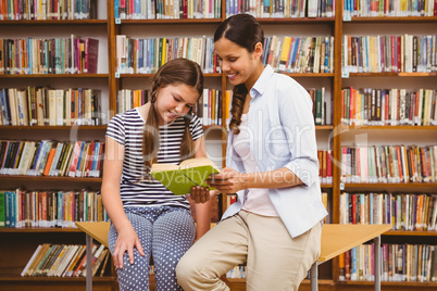 Teacher and girl reading book in library