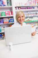 Smiling pharmacist using laptop and holding prescription