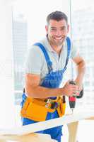 Happy handyman drilling plank in office