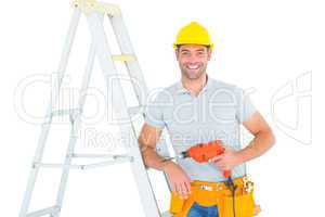 Happy handyman with power drill leaning on ladder
