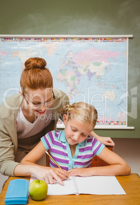 Teacher assisting little girl with homework in classroom
