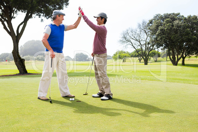 Golfing friends high fiving on the hole