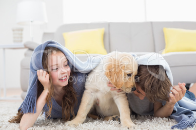 Siblings with puppy under blanket lying on rug