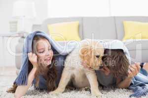 Siblings with puppy under blanket lying on rug