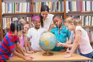 Cute pupils and teacher looking at globe in library