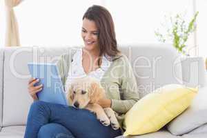 Beautiful woman with dog using digital tablet on sofa