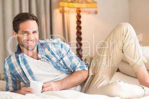 Handsome man relaxing on his bed with hot drink