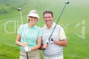 Golfing couple smiling at camera holding clubs