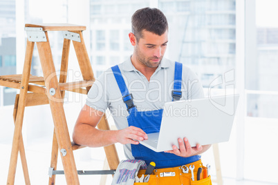 Repairman using laptop by ladder in office