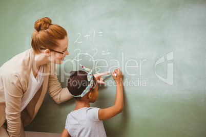 Teacher assisting girl to write on blackboard in classroom