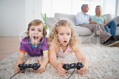 Siblings playing video game while parents sitting on sofa