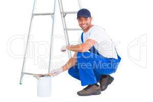 Portrait of happy handyman crouching by paint can