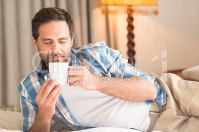 Handsome man relaxing on his bed with hot drink