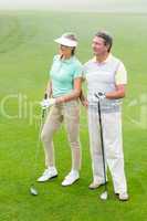 Golfing couple smiling and holding clubs