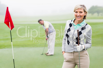 Lady golfer smiling at camera with partner behind