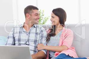 Couple looking at each other while using laptop