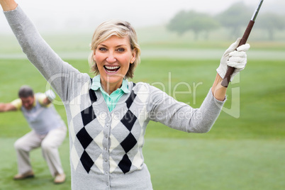 Lady golfer cheering at camera with partner behind