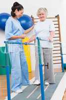 Senior woman walking with parallel bars with therapist