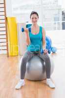 Smiling young woman exercising with dumbbells on fitness ball