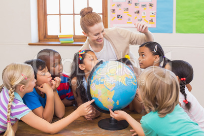 Cute pupils and teacher in classroom with globe