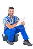 Handyman writing on clipboard while sitting on toolbox