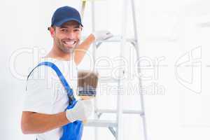Happy handyman with paintbrush while climbing ladder