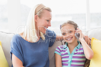 Mother looking at daughter using mobile phone on sofa