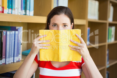 Student covering face with book in library