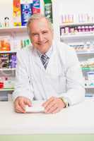 Senior pharmacist leaning on the counter holding prescription