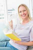 Happy woman having coffee while reading book on sofa