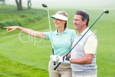 Golfing couple smiling and holding clubs