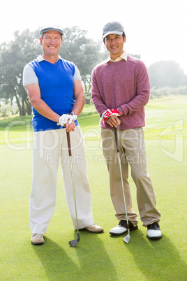 Golfing friends smiling at camera holding clubs