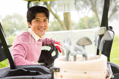 Happy golfer driving his golf buggy smiling at camera