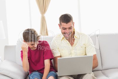 Father and son with laptop sitting on sofa