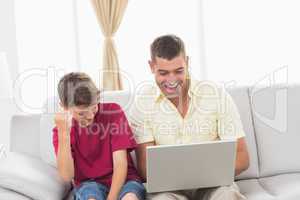 Father and son with laptop sitting on sofa