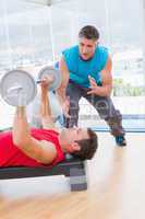 Trainer assisting man with dumbbells