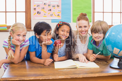 Cute pupils and teacher smiling at camera in classroom