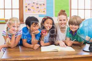 Cute pupils and teacher smiling at camera in classroom